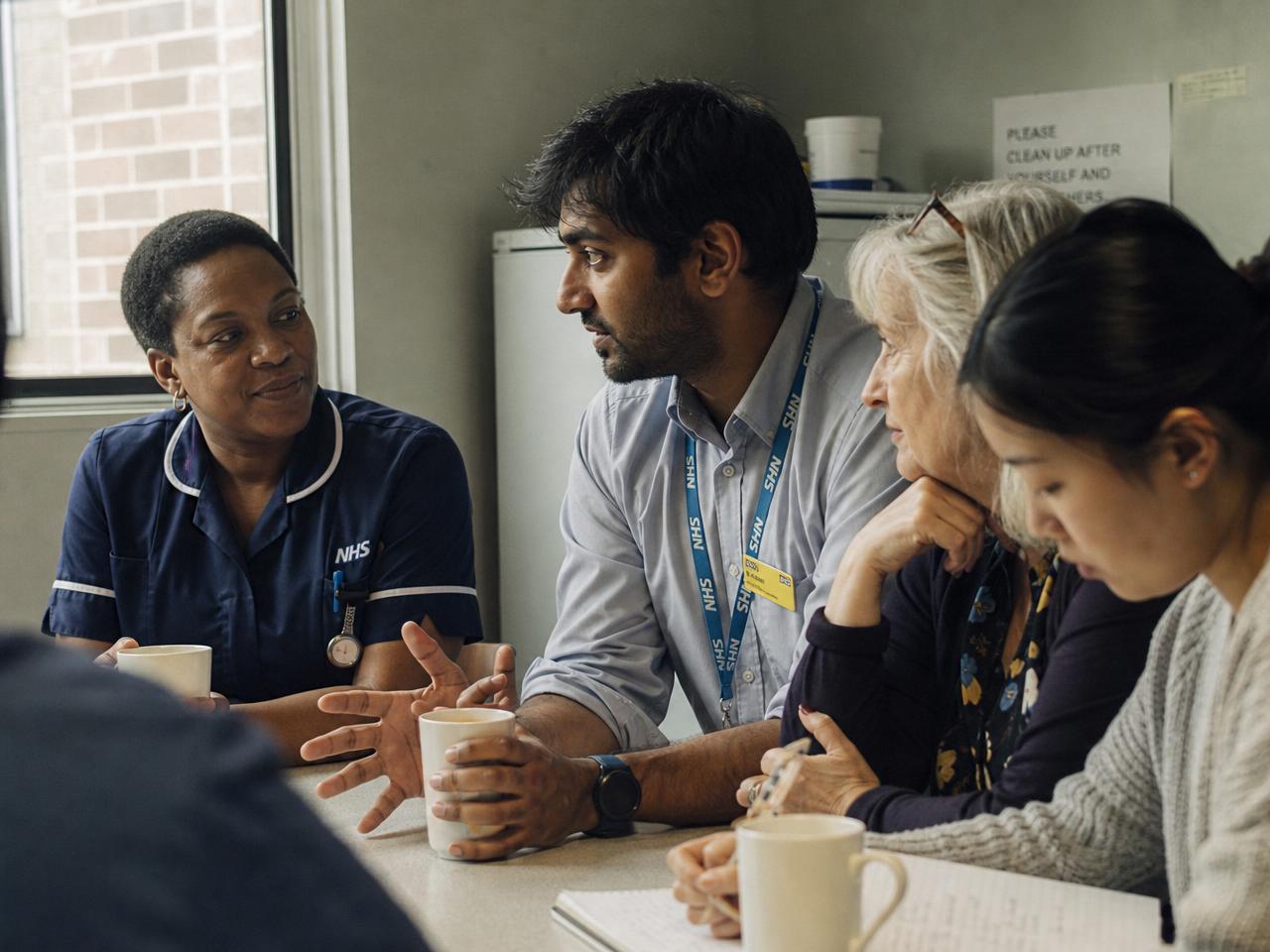 NHS colleagues from different backgrounds talking over mugs of tea in a hospital staff room